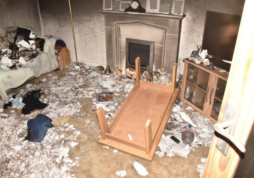 The crime scene of a living room after a fire, with debris covering the floor and an upturned coffee table.