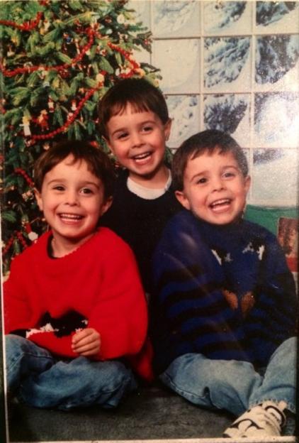 Triplets Quentin B, Andrew A, and Joel C Meloff as children, sitting in front of a Christmas tree.
