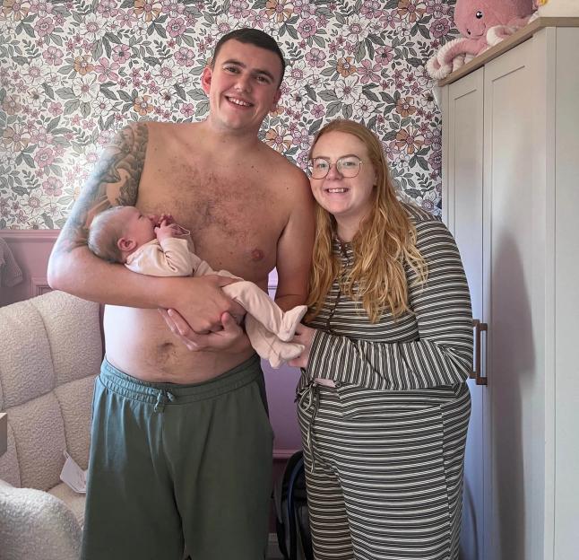 Jake Watts, his partner Chloe, and their daughter Orla Ann smile at the camera.