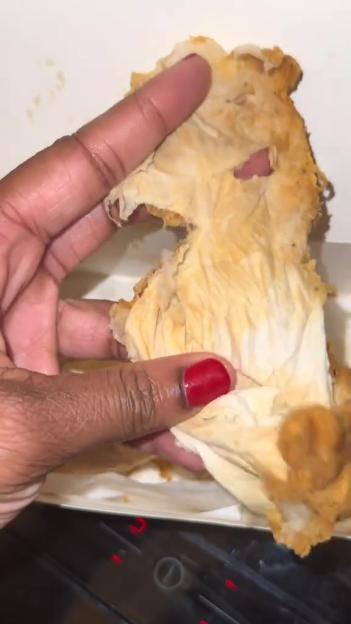 A hand pulling apart a fried chicken wing, revealing uncooked meat inside.