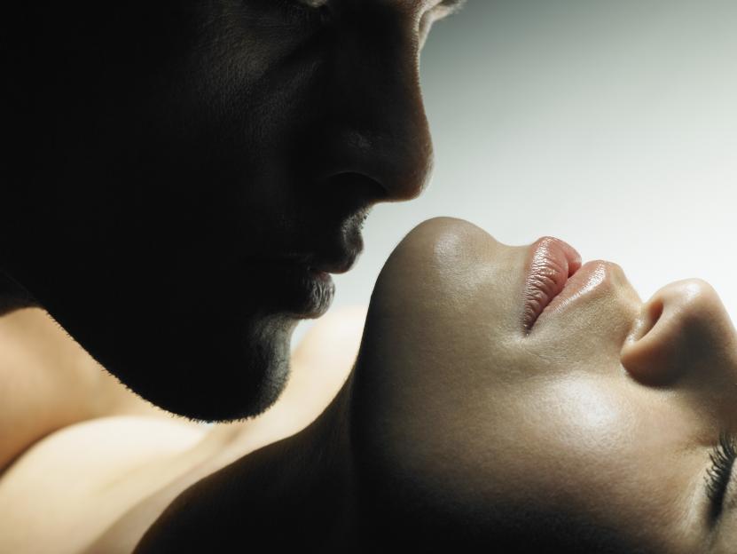 A dark silhouette of a man's face leaning into a woman's face, about to kiss her.