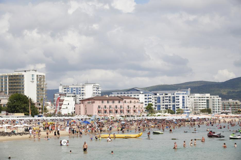 a crowded beach with a pink building in the background