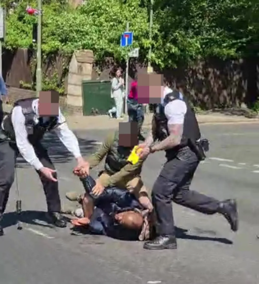 Four police officers apprehending a person lying on the ground.