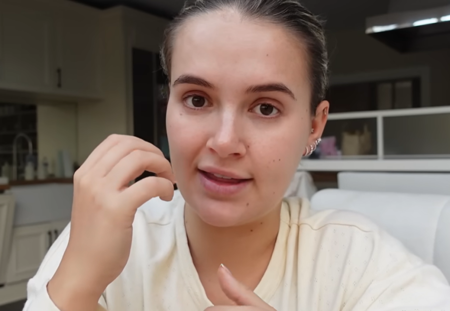 Molly-Mae Hague speaking, her hair pulled back, wearing a light-colored top, with her hand near her chin.