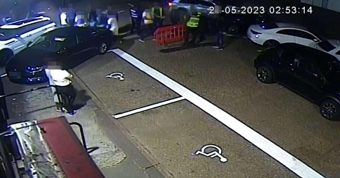 CCTV footage of a car near a group of people and parked cars in a parking lot.