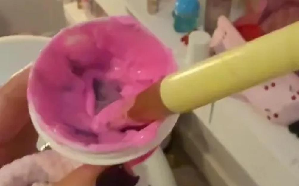 A hand dipping a finger into a pot of pink goo.