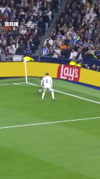 A football player in a white uniform prepares to take a corner kick during a UEFA Champions League match.