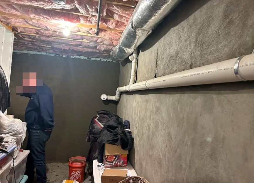 A person standing in a dimly lit basement with exposed insulation and pipes.