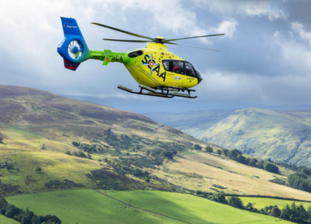 Scotland's Charity Air Ambulance helicopter flying over green hills.