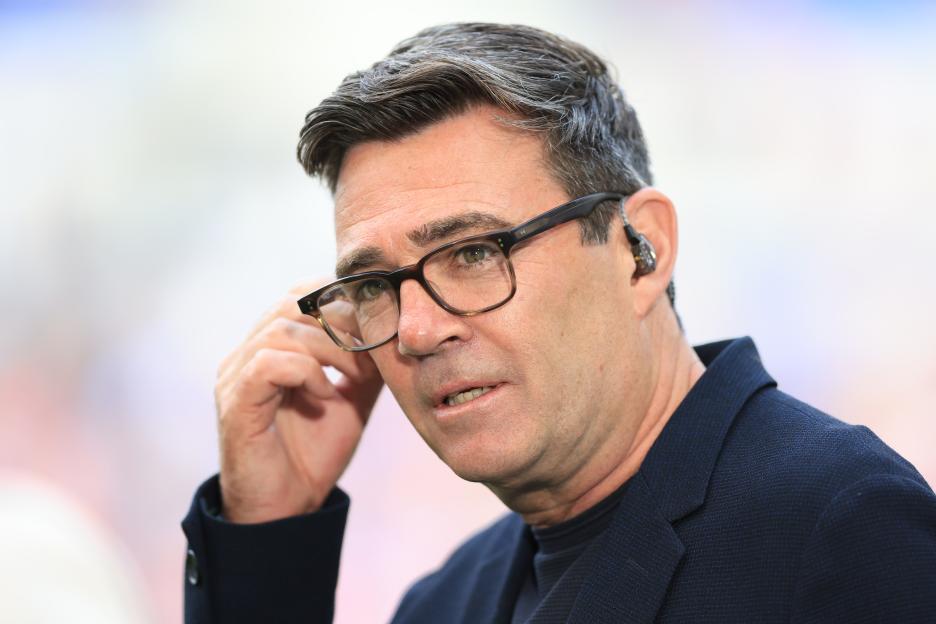 Andy Burnham wearing glasses and an earpiece, touching his glasses.