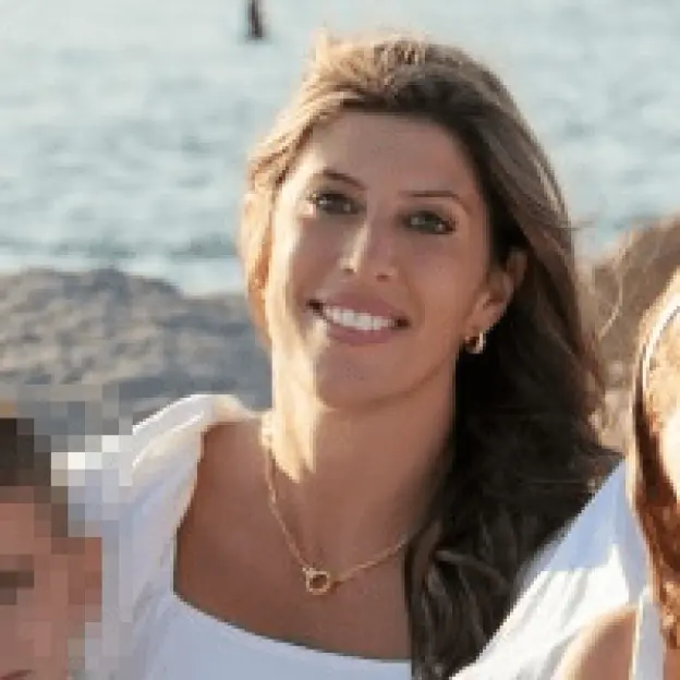 A smiling woman with long brown hair and a white top.