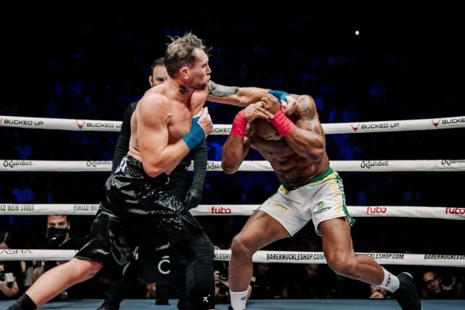Two male boxers fighting in a ring, one throwing a punch to the other's head.