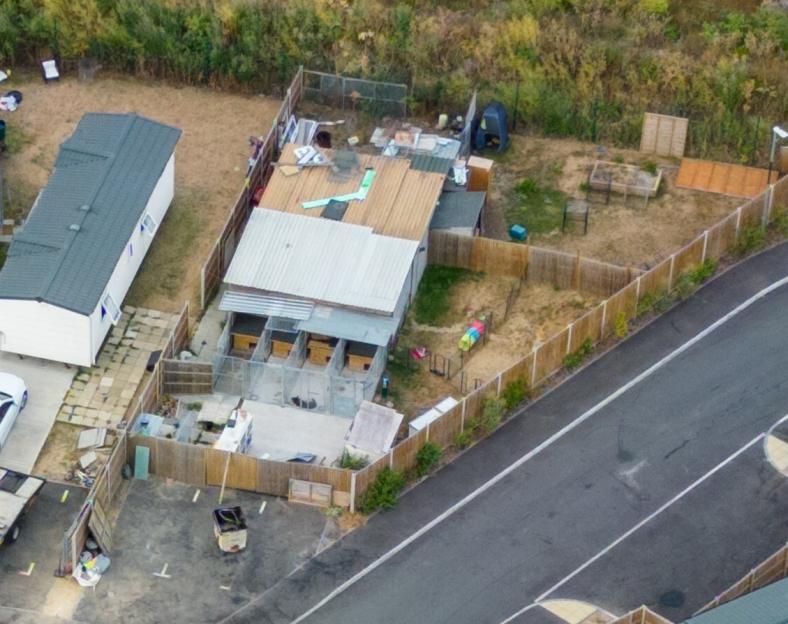 Aerial view of a circular residential area with houses and numerous caravans, some with small swimming pools or trampolines, surrounded by unkempt fields.