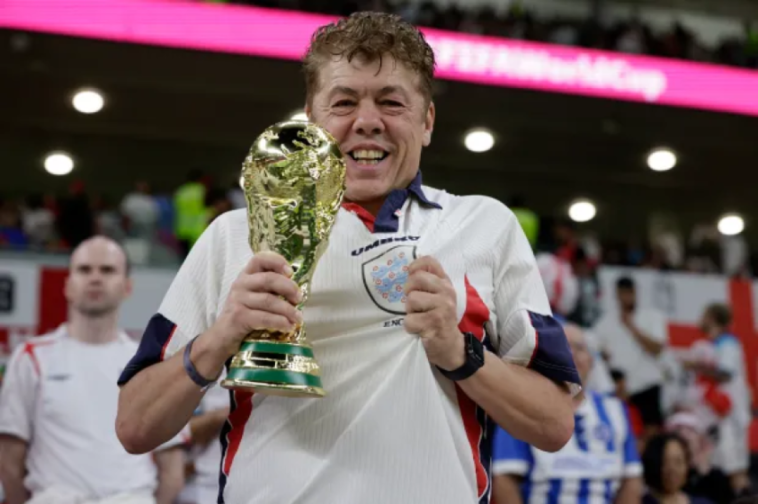 a man in an umbro shirt holds up a trophy