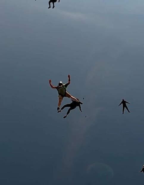 Two skydivers collide in mid-air, with others freefalling around them against a dark sky.