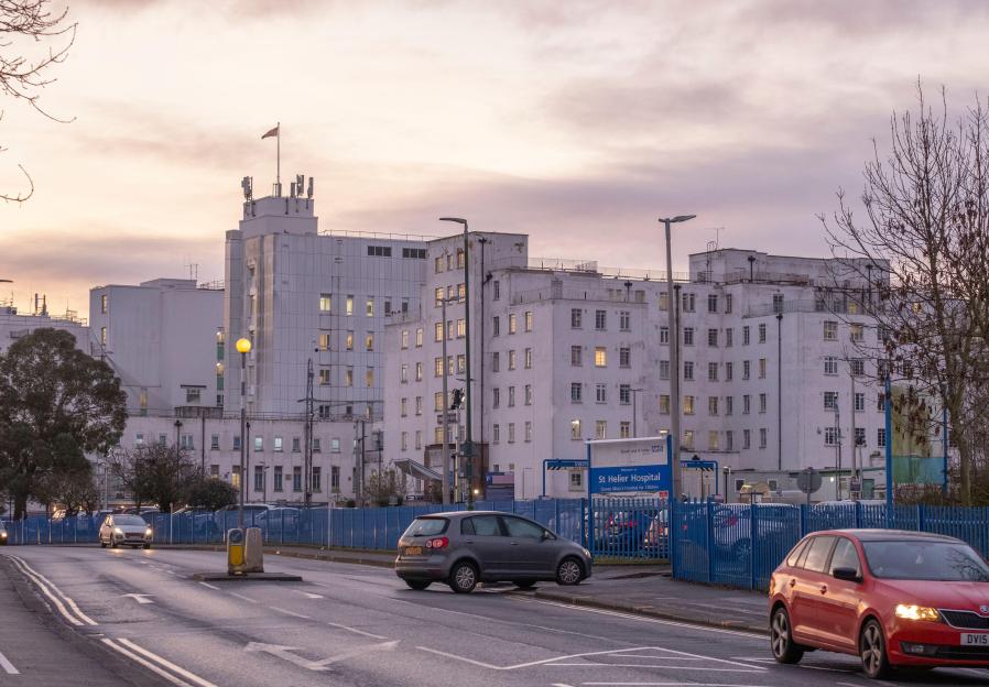 An early morning view of St Helier Hospital, a major NHS hospital in South London, with several cars on the road in the foreground and a visible sign for the hospital.