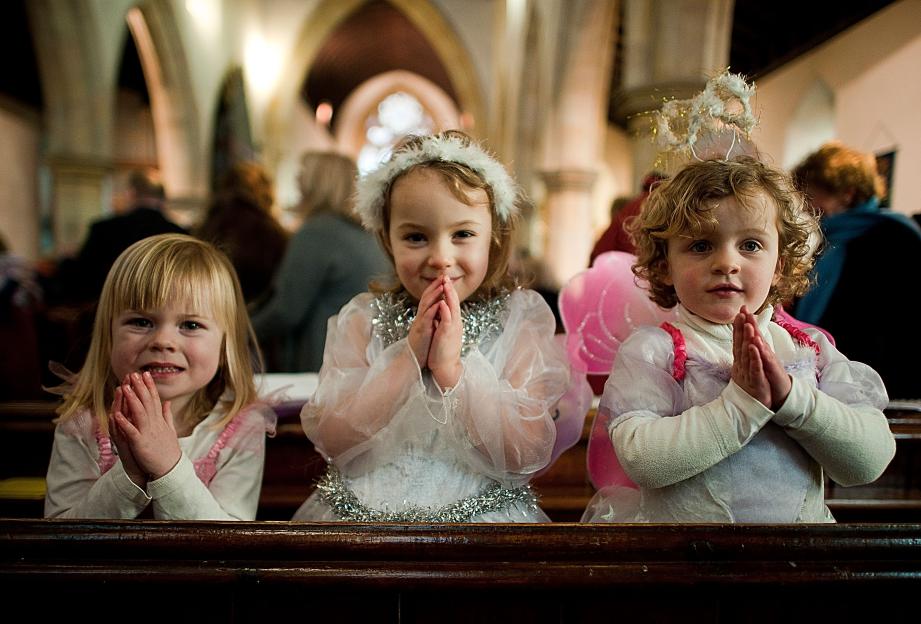 Three young girls dressed as angels wait for their cue during a traditional Christmas Nativity.