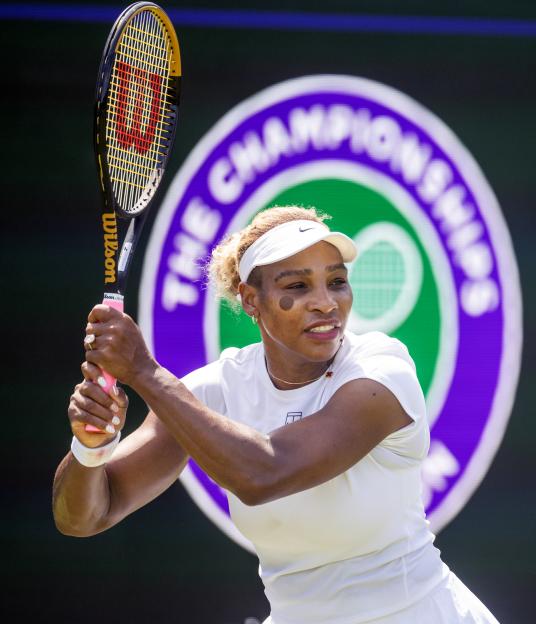 Serena Williams in a white visor, shirt, and skirt, holding a tennis racket.