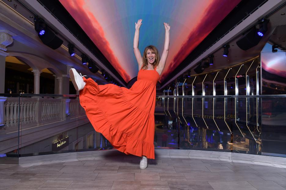 Shirley Ballas on a cruise, wearing a long orange dress, with her arms raised in excitement.