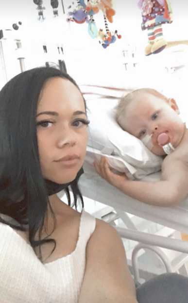 A woman takes a selfie with her infant daughter Elena in a hospital bed, who is recovering from a burn injury.