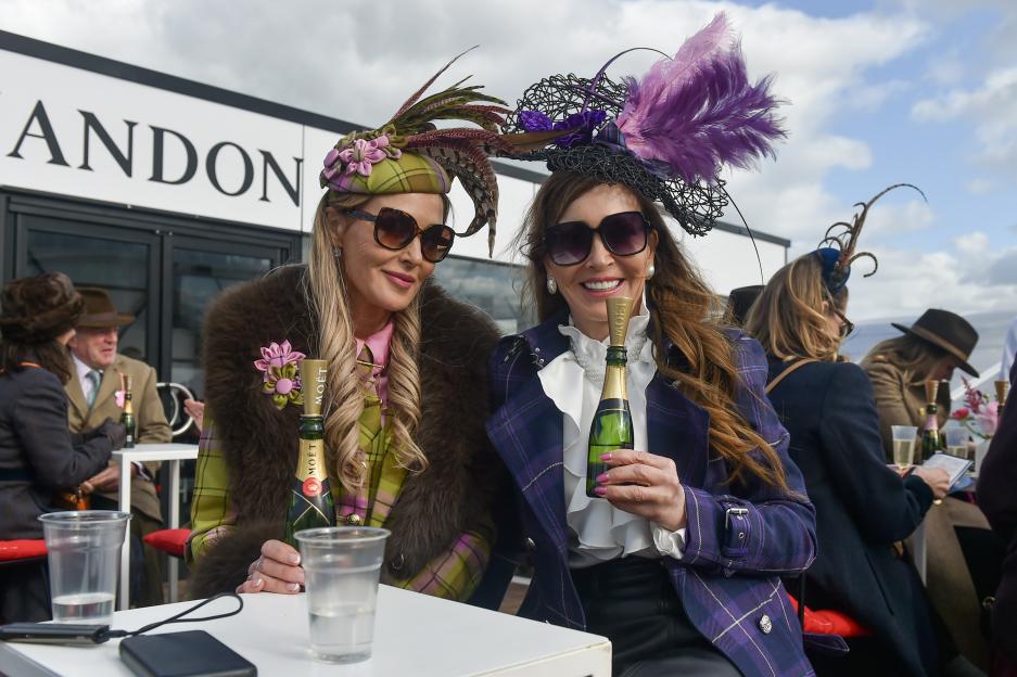 Two women in hats and sunglasses holding mini bottles of Moët champagne at the Cheltenham Festival races.