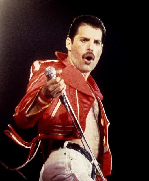 Freddie Mercury singing into a microphone on stage, wearing a red jacket and white pants.