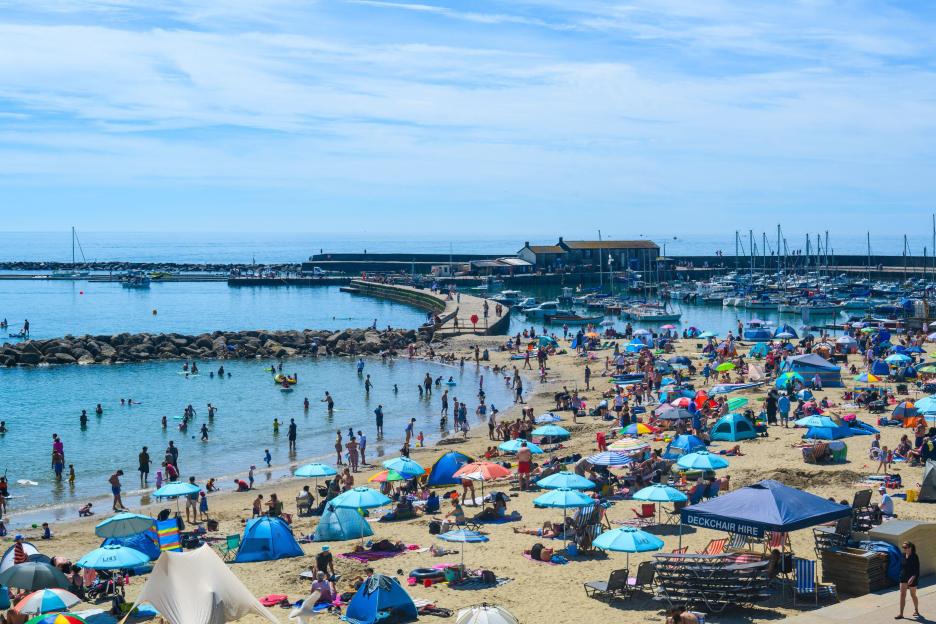 Lyme Regis, Dorset, UK. 21st June, 2026. UK Weather: Sunbathers and families flock to the packed beach at the seaside reesort of Lyme Reigs to bask in hot sunshine on the first day of Astronomical Summer. Temperatures are set to soar across the UK th