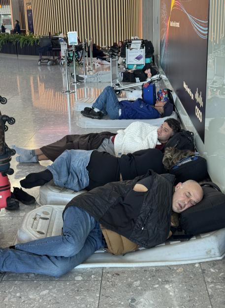 People sleep on the floor and on luggage carts in Heathrow Airport's Terminal 5 due to flight delays.