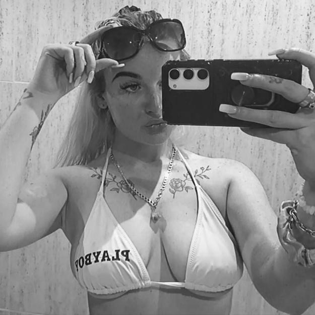 Black and white mirror selfie of Hannah Metcalfe in a bikini top with "PLAYBOY" written backwards.