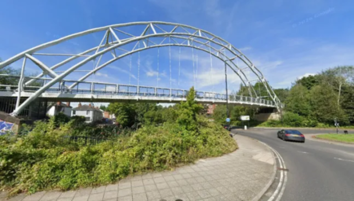 Millennium Bridge, with surrounding roads and foliage, under a blue sky.
