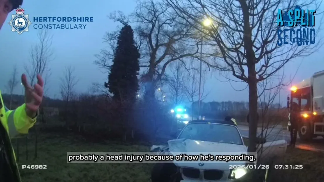 Dashcam footage of the aftermath of a car crash involving a heavily damaged white car, emergency vehicles, and police officers.
