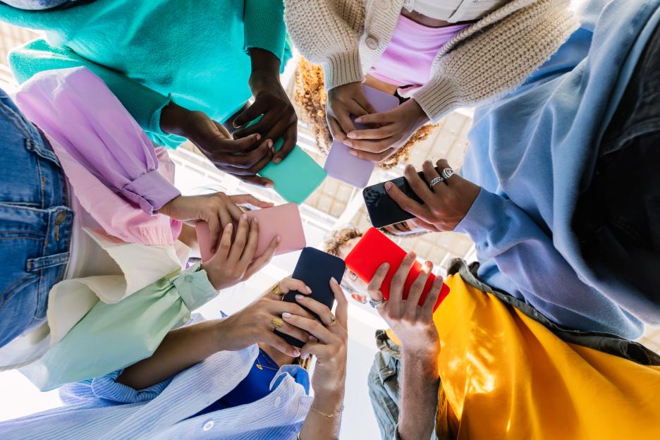 Low-angle view of a diverse group of young people holding smartphones in a circle.