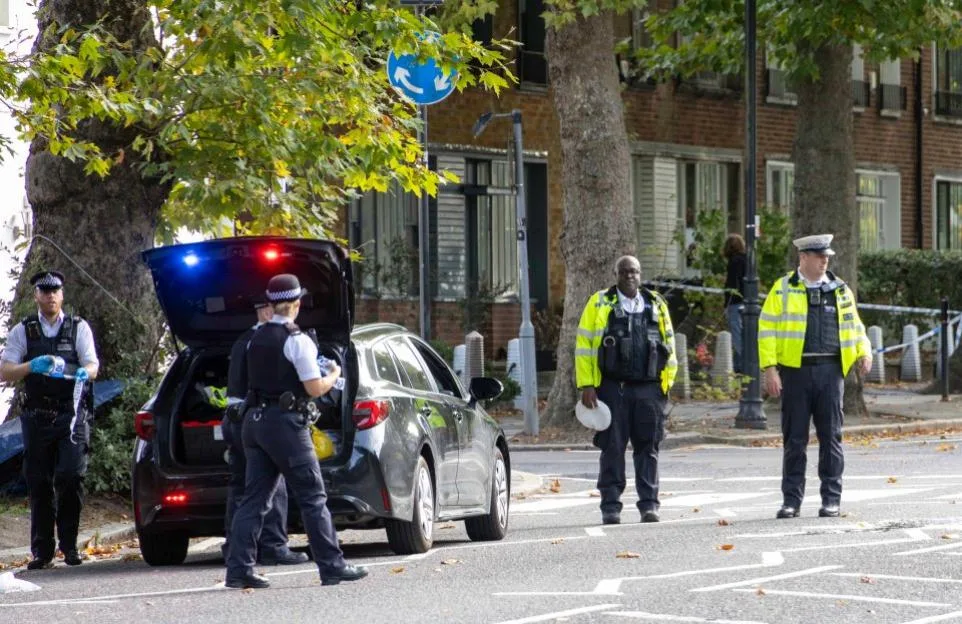 Police officers at a crime scene with a vehicle and a blue and white striped barrier.