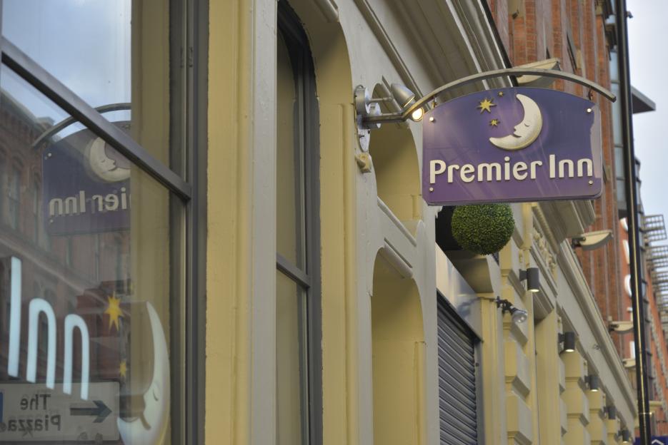 A purple Premier Inn sign with a sleeping moon and stars, attached to a building.