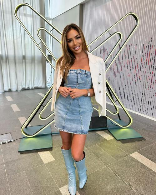 a woman in a denim dress and boots stands in front of a paper clip sculpture