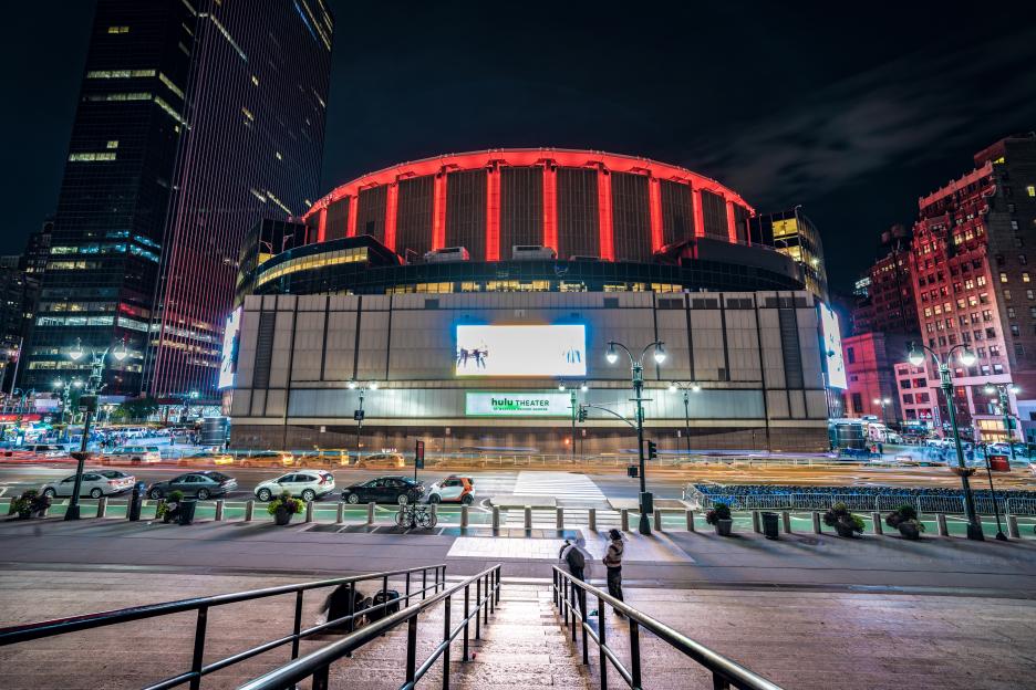 Night view of Madison Square Garden, an arena in Midtown Manhattan with red illuminated arches on its roof.