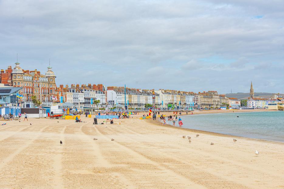 Seaside view of the English town Weymouth, with a sandy beach and buildings along the coast.