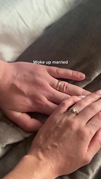 A close-up of two hands, one with a plain band and the other with an engagement ring and wedding band, intertwined with the text "Woke up married."