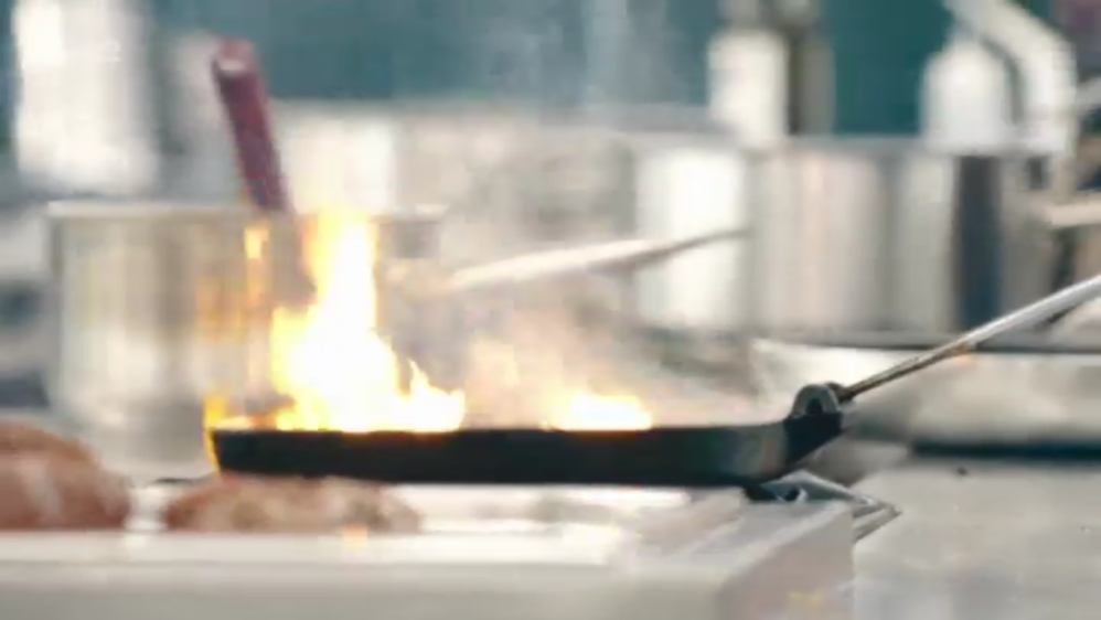 Searing food with a pan on fire in a kitchen setting.