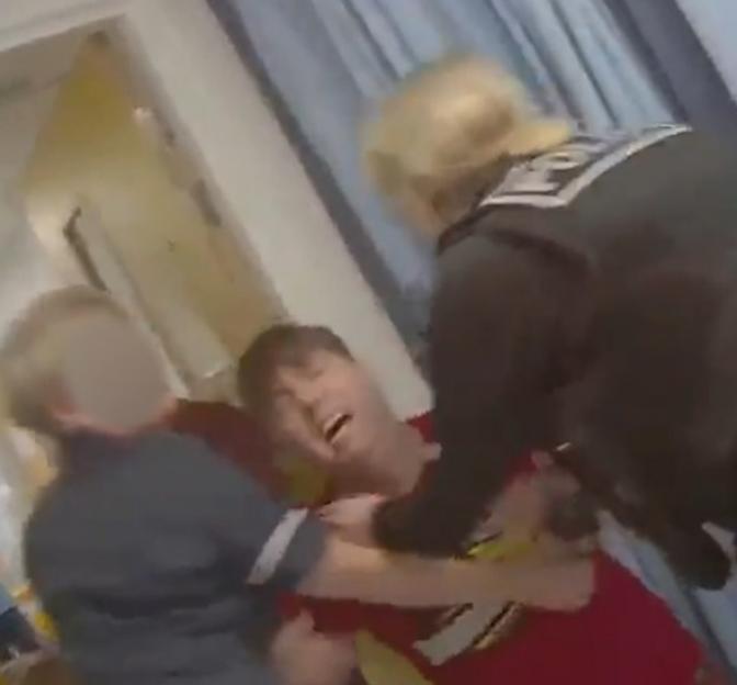 A man in a red shirt being restrained by two people in a hallway.