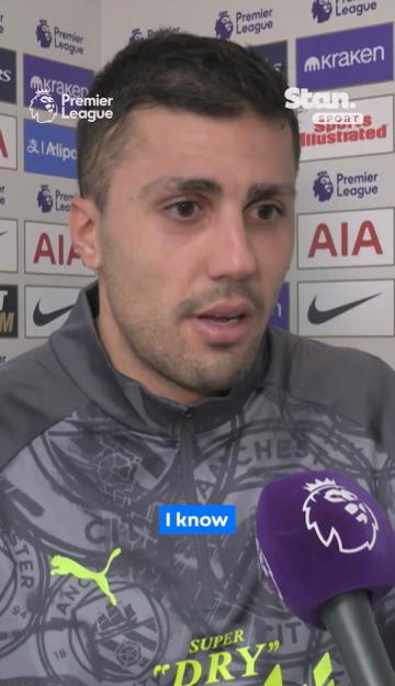 Man speaking into a purple microphone with "Premier League" logo.