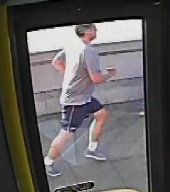 CCTV image of a jogger in a grey shirt and black shorts, running.