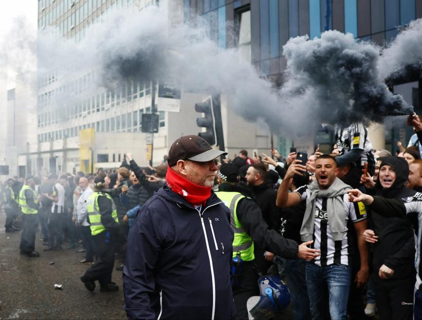 Newcastle United and Sunderland fans gathering outside a stadium before a match, with smoke in the air.