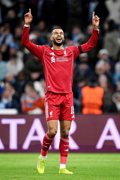 A Liverpool FC player in a red jersey with his arms raised in celebration during a match.