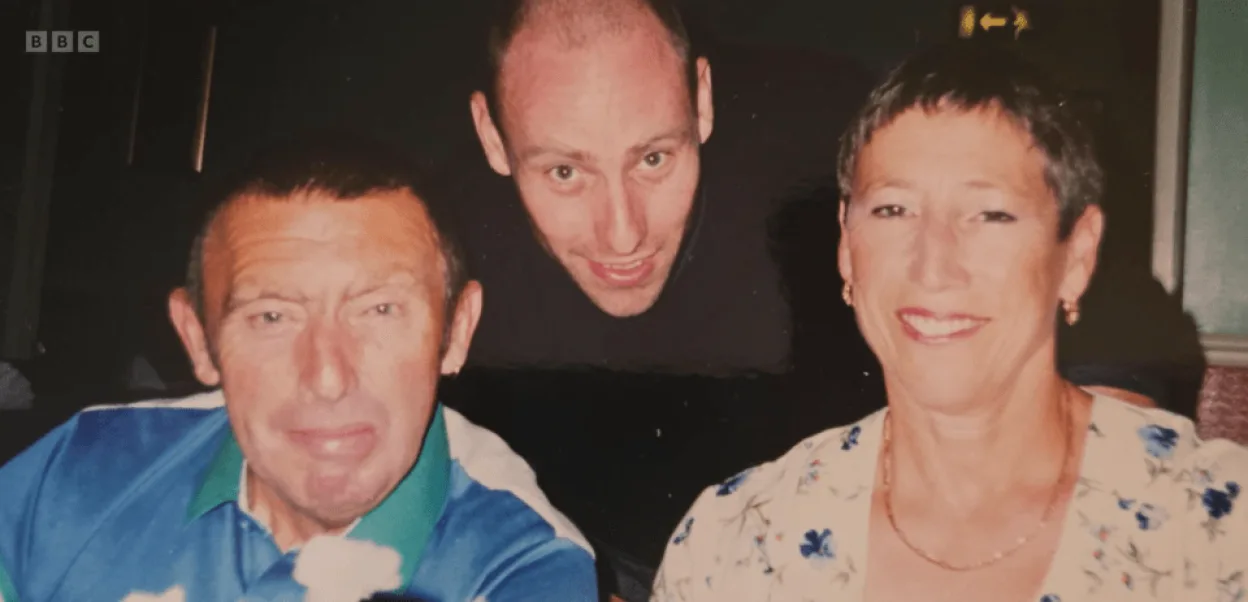 Three people smiling at the camera, a man in a blue and green polo shirt on the left, a woman in a floral shirt on the right, and a man in a black shirt behind them.
