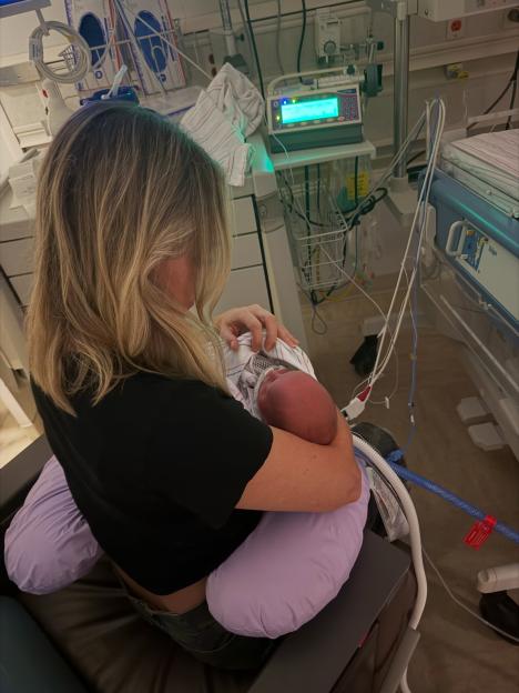 A woman holding a newborn baby in a hospital room, surrounded by medical equipment.