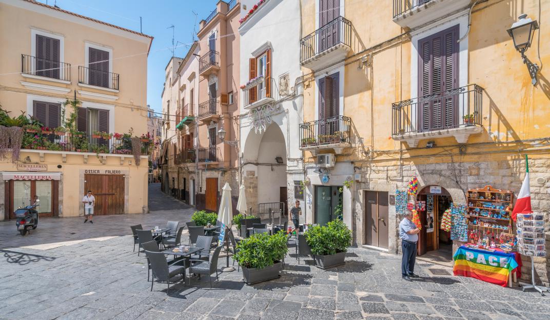 Old town square in Bari, Puglia, Italy, with historic buildings, a cafe, and a souvenir stand.