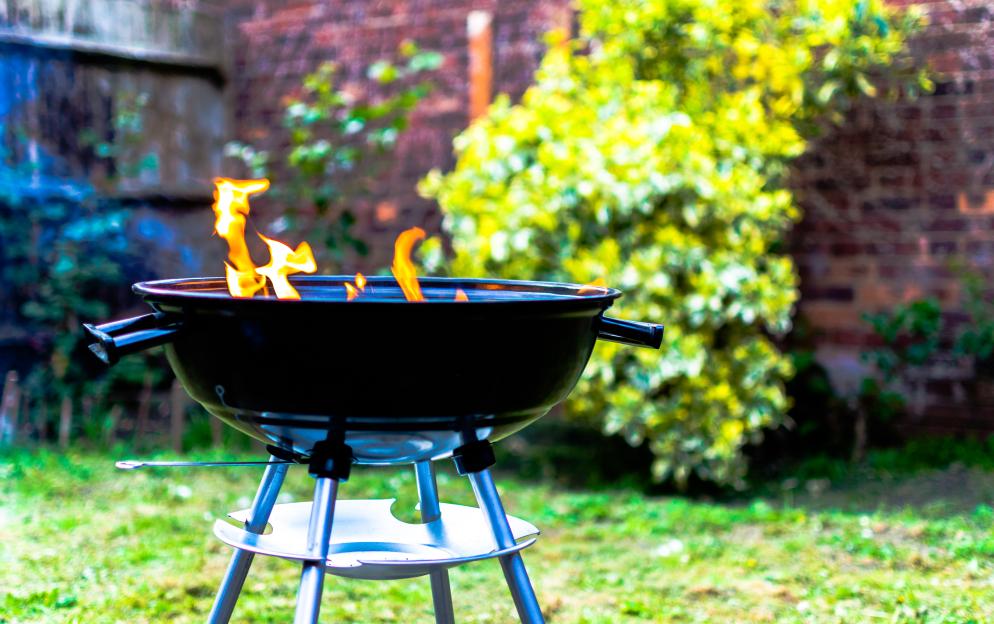 Flames rise from a black kettle grill in a backyard.