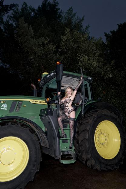 Woman in lingerie and stockings posing on the steps of a John Deere tractor.