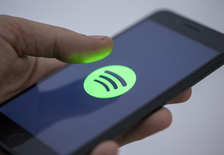 A person's finger hovering over the Spotify logo on a smartphone screen.